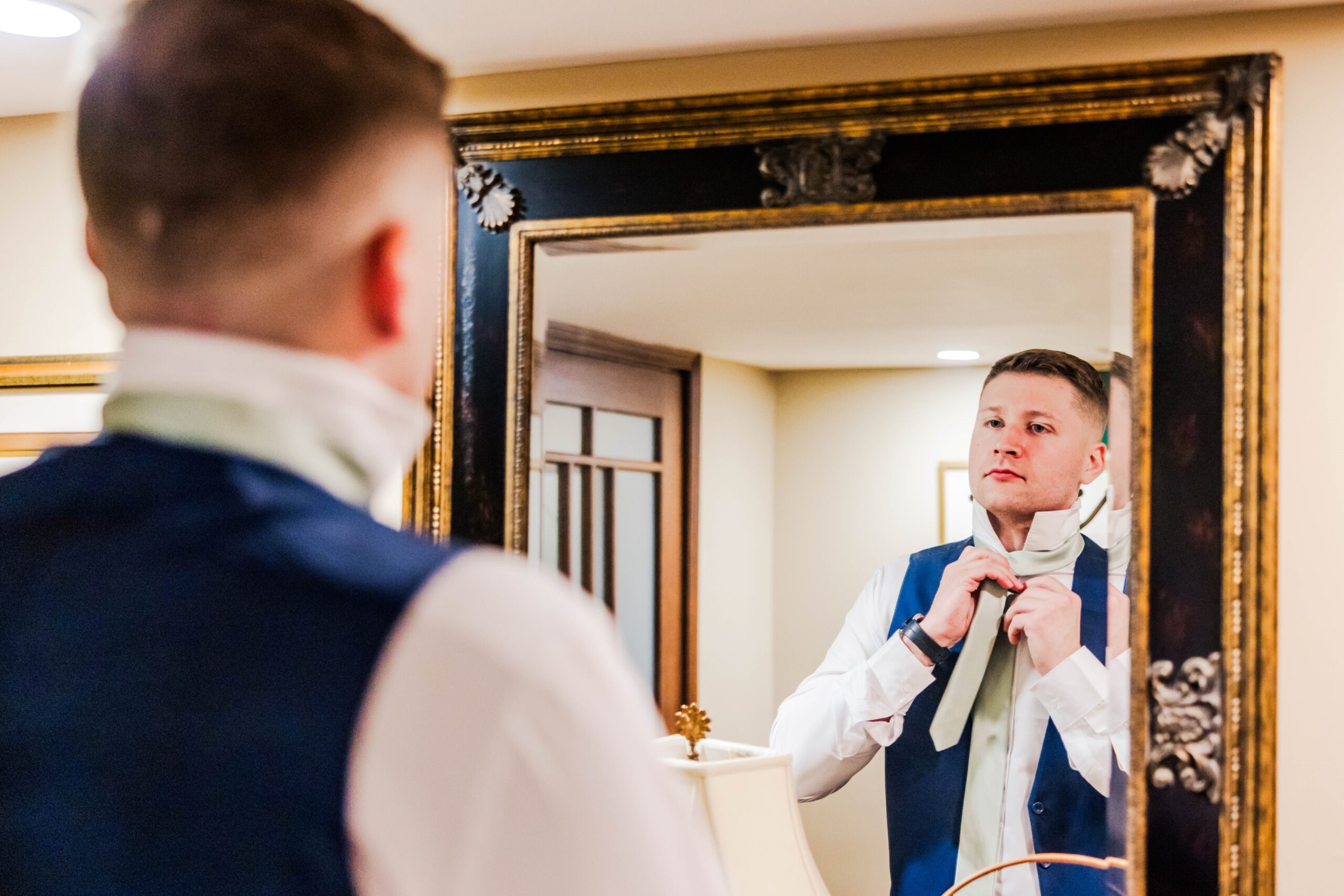 Groom staring in the mirror while adjusting his tie