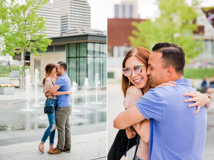 Man in blue polo shirt and woman in torn blue jeans and pink off the shoulder shirt hugging in front of water fountains in downtown cincinnati ohio