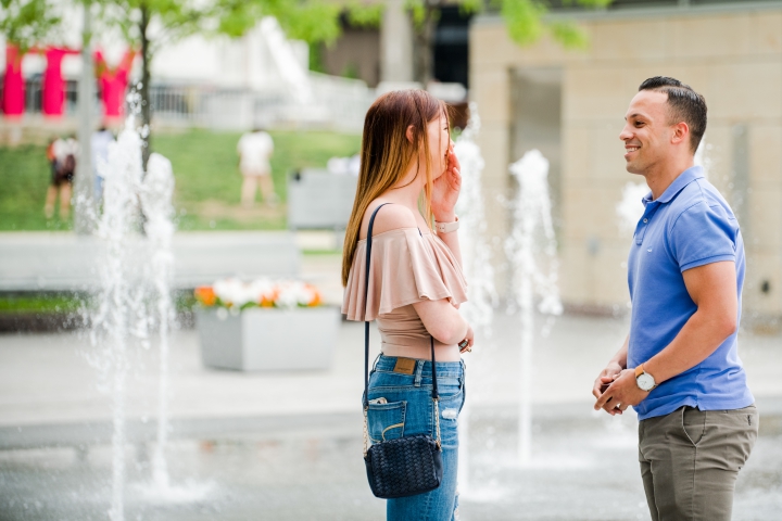Shocked woman standing near water fountain as man holds engagement ring box downtown cincinnati