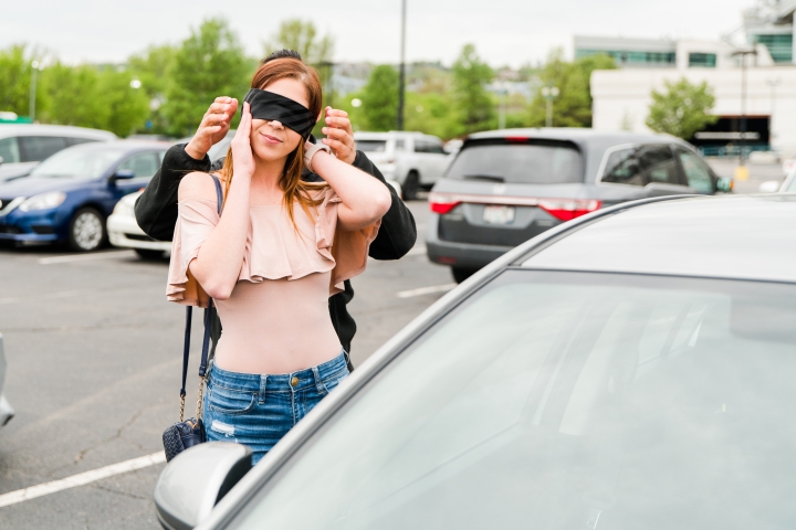 Man blindfolds young woman in parking lot with black tie