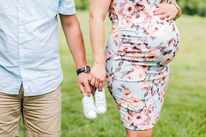 Hispanic man and pregnant woman  in a blue floral dress each holding a white baby converse shoe