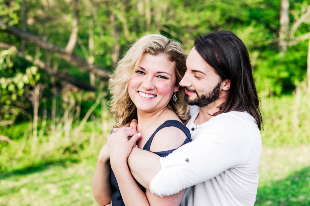 Stacy smiling for the camera while Joseph hugs her during their spring engagement session