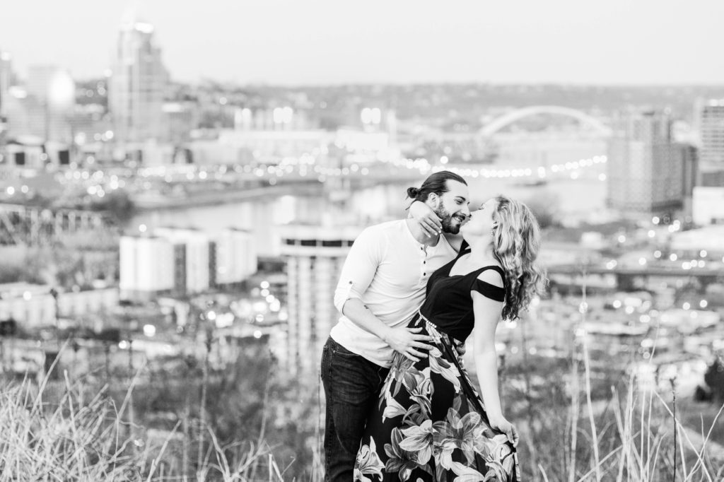 Black and white photo of the couple about to kiss with the cityscape in the background 