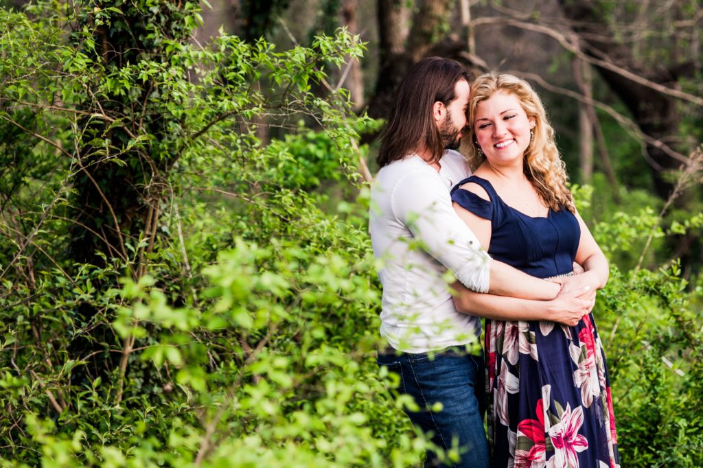 Joseph hugging Stacy from behind in front of a tree during their spring engagement session