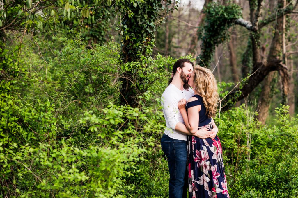 The couple kissing in front of some greenery during their spring engagement session