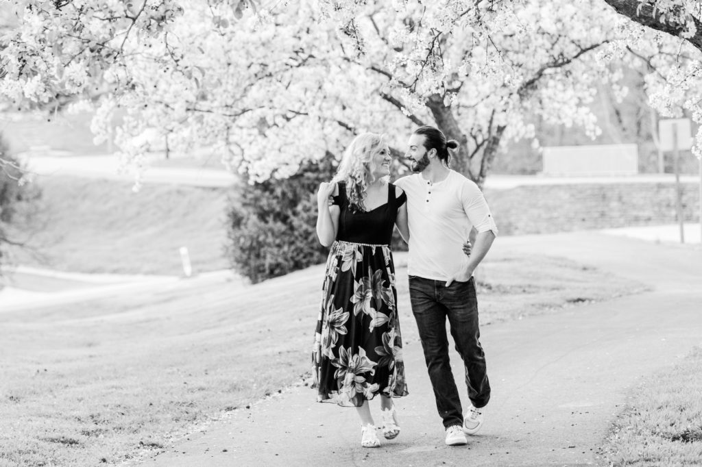 Black and white photo of Stacy and Joseph walking along a path under a flowering tree during the couple's spring engagement session