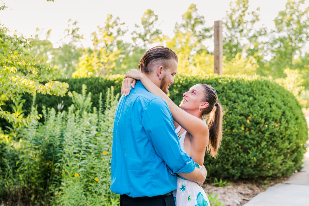 A couple captured hugging in front of some bushes during an engagement photography session done by two engagement photography pros.