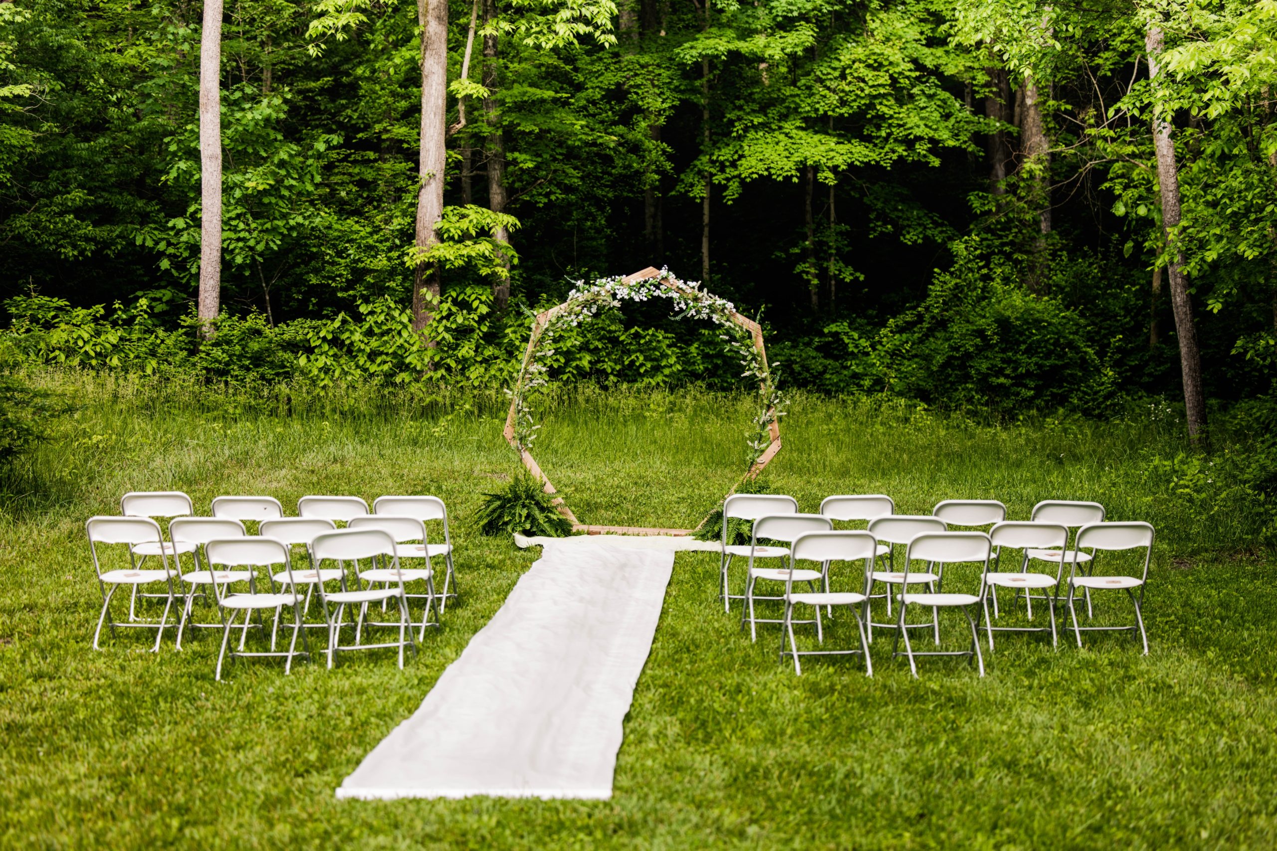 Outdoor wedding ceremony space with white chairs and floral archway in an open field in front of wooded area at Hueston Woods.