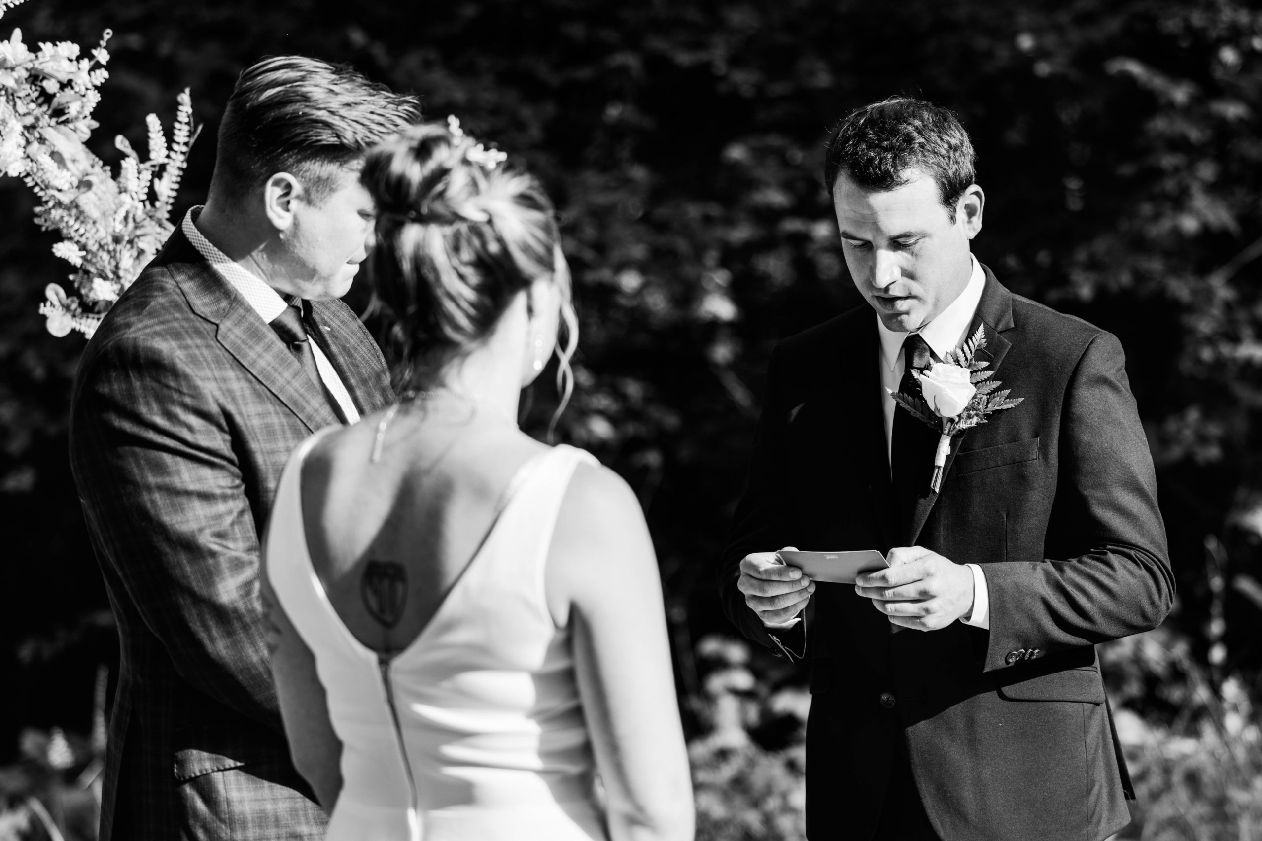 Black and white photo of the groom, Ross, reading his vowels to his bride, Abby at the alter.