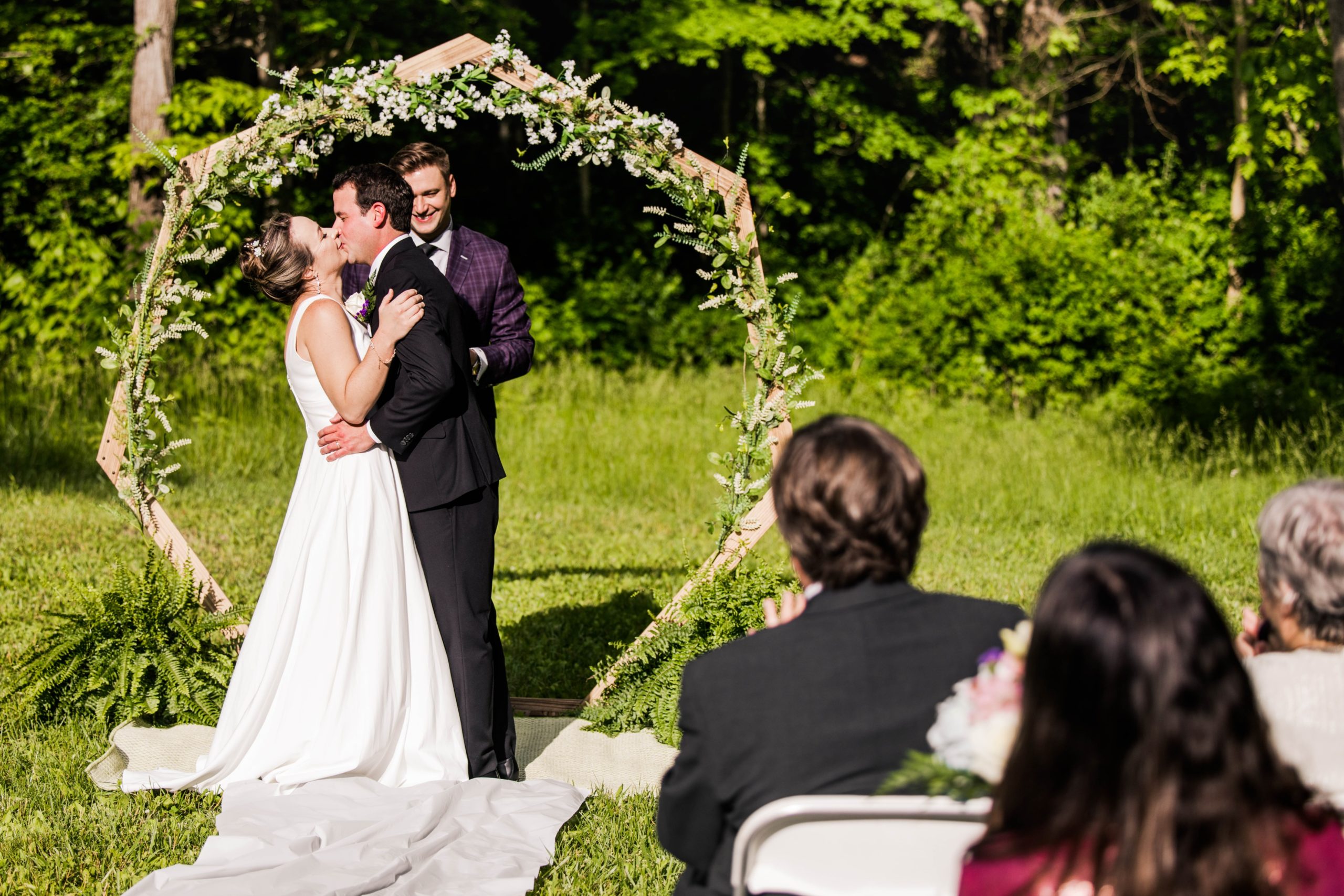 Distant photo of Abby and Ross sharing their first kiss at the alter at Hueston Woods while their guest are clapping.