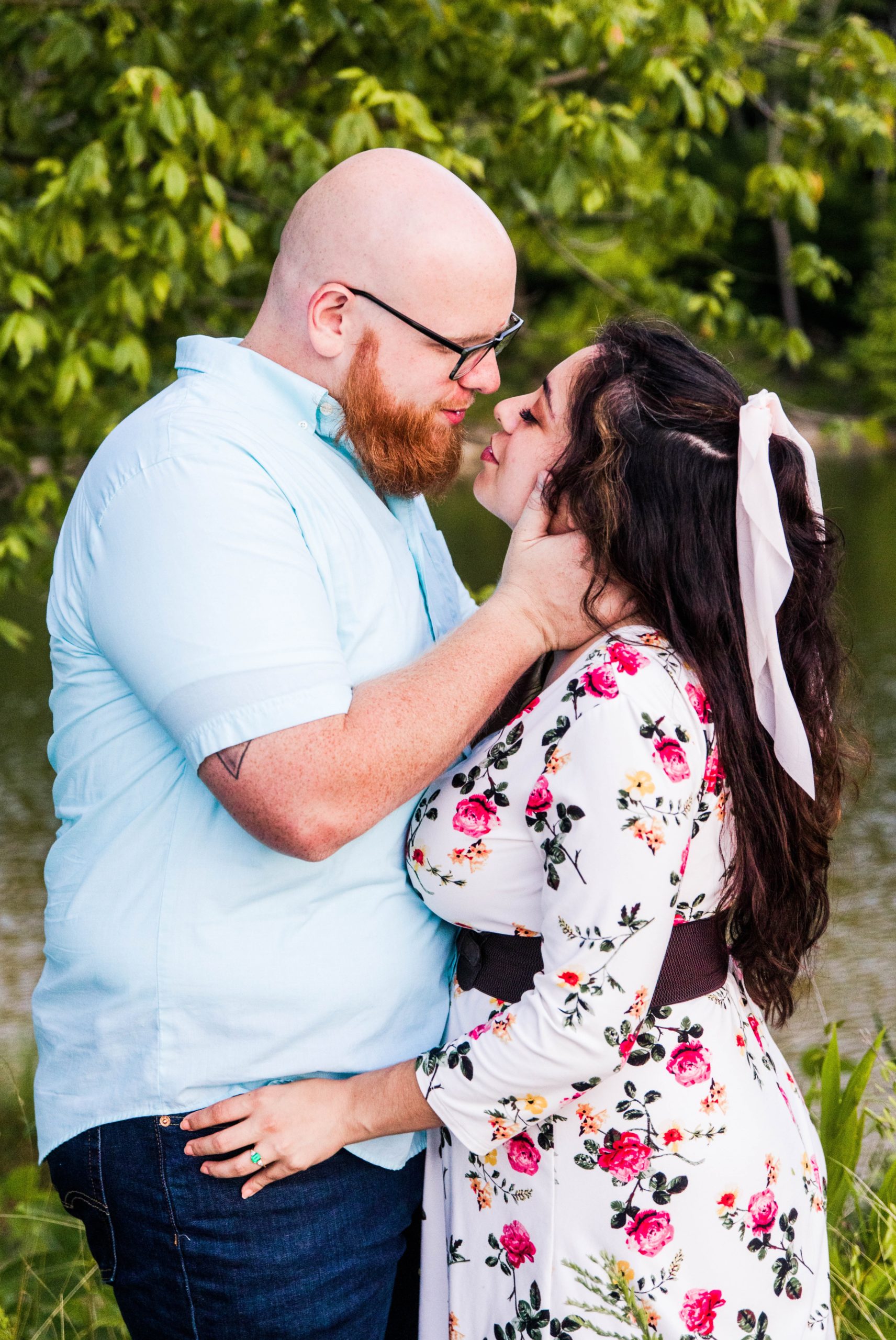 Summer time Cincinnati engagement session with a groom's hand holding onto the side of the bride's face as they lean closer for a kiss