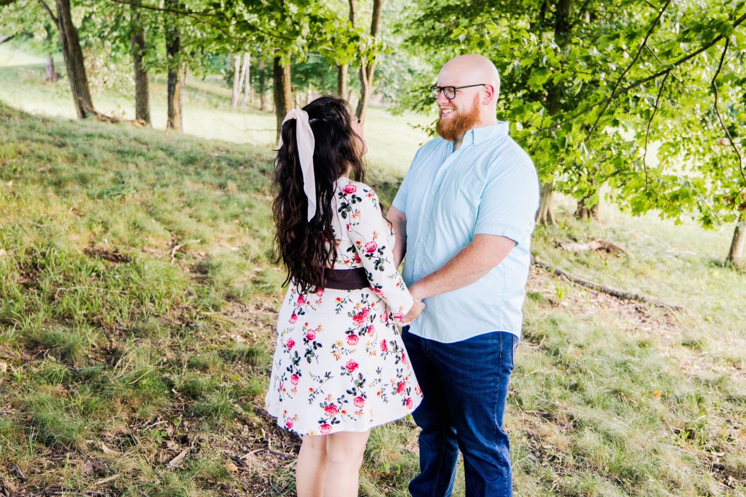 Engaged couple holding hands facing each other smiling at in a a grove of trees at East Fork State Park