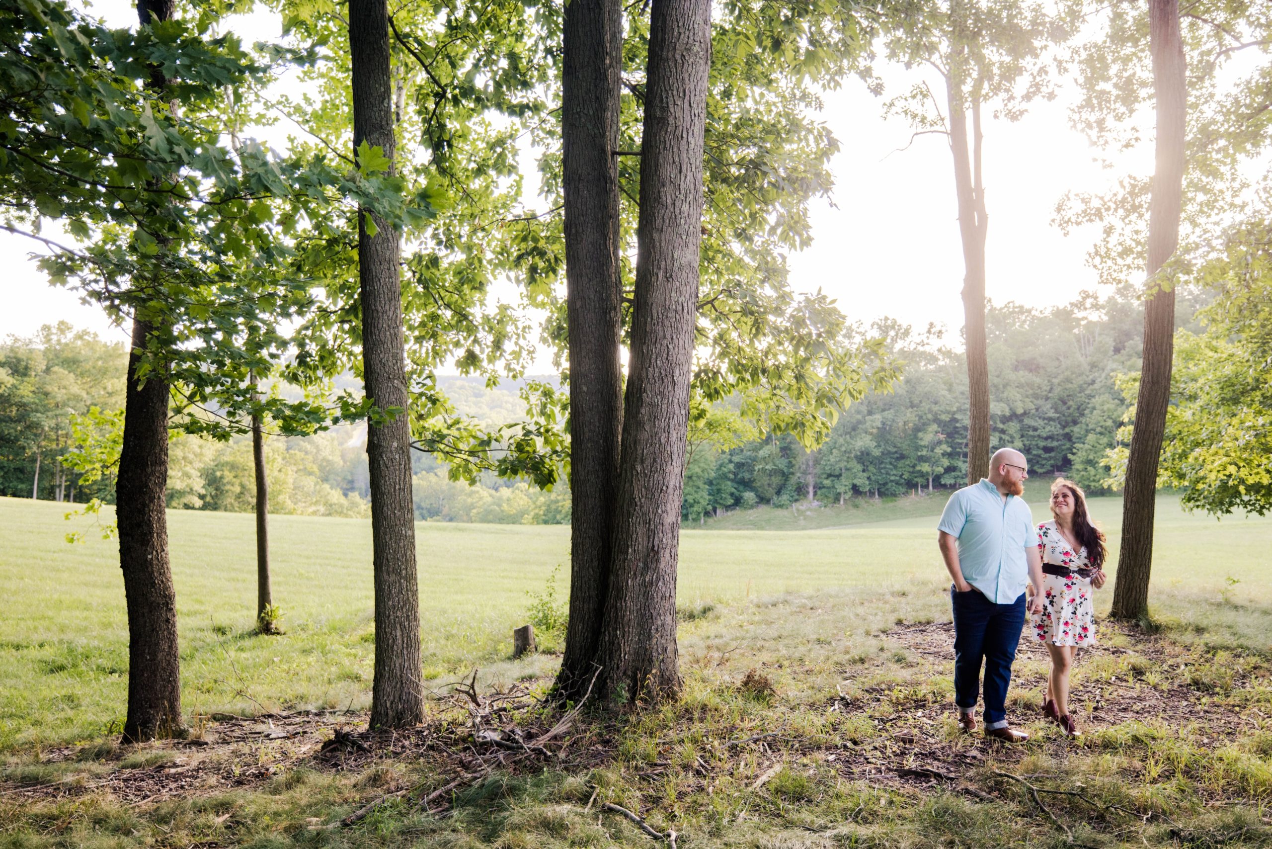Couple entering a grove of trees at East Fork State Park looking at each other for their summer engagement photos.