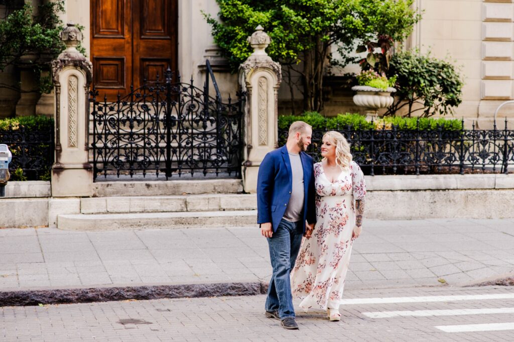 Engaged couple looking at each other as they cross the street in front of a historic house in downtown cincinnati