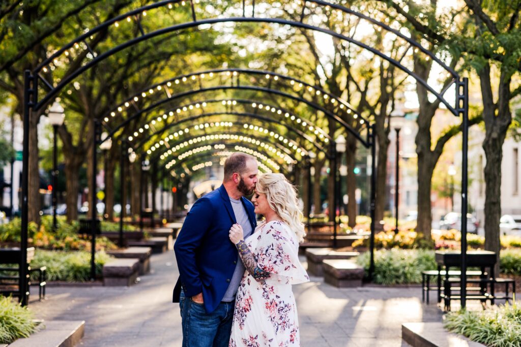 Man kissing woman's forehead as she holds onto his suite jacket at Piatt Park in Downtown Cincinnati at sunset