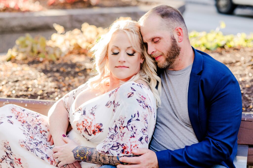 Engaged couple of a man and woman sitting on a park bench at sunset cuddled into each other in downtown cincinnati