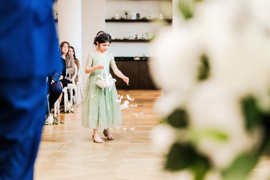 Flower girl in a green dress concentrating on distributing petals down the aisle. 
