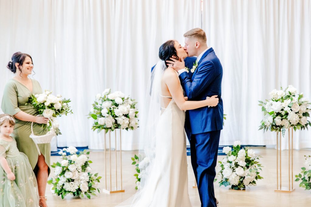 Bride and groom sharing their first kiss at an alter with white florals and greenery