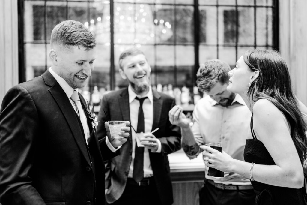 Groom enjoying a cocktail during the reception surrounded by 3 friends all laughing