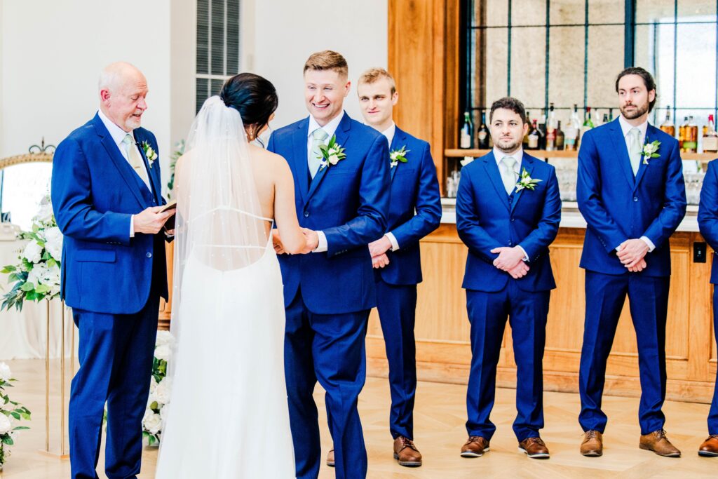 Groom smiling at the bride at the alter with is groomsmen looking at him. 