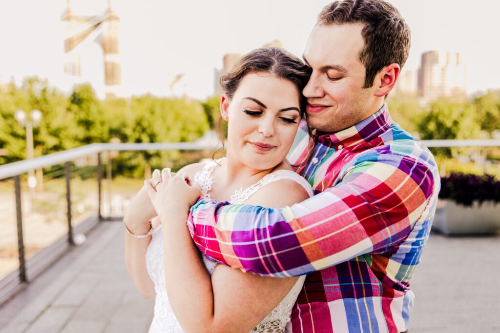 Man hugging woman from behind will smiling down at her during engagement session