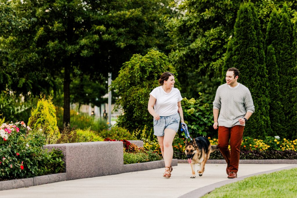 Loving couple at Smale Park Rose Garden running and smiling with their german shepherd