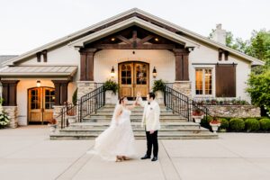 A couple dances gracefully in front of a large manor house event center, featuring rustic stone steps and charming wooden accents.